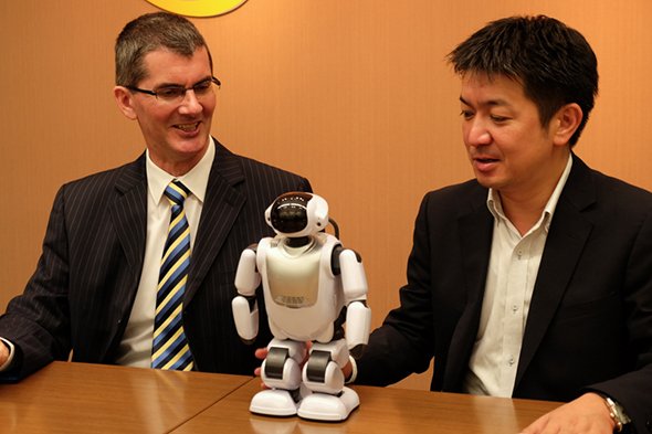 日本セーフネットのIDSSソフトウェアマネタイゼーション事業部Vice Presidentのジェラード・ポールクラーク氏（左）とDMM.com ロボット事業部事業部長の岡本康広氏（右）。中央はDMM.make ROBOTSで販売されている富士ソフト製コミュニケーションロボット「Palmi」