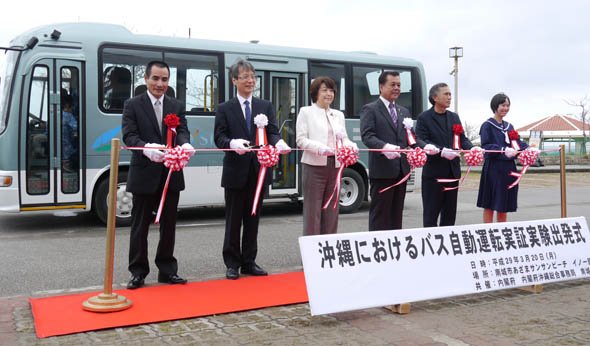 自動走行バス実証実験の出発式には、多くの関係者や報道機関が集まった。写真は、沖縄担当大臣補佐官の島尻安伊子氏や内閣府沖縄総合事務局長、南城市長、地元区長などによるテープカットの様子